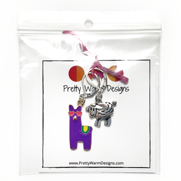 Purple enamel llama crochet stitch marker with pink heart eyes and yellow and green accents plus antique silver lamb locking crochet stitch marker attached with pink yarn to cardstock with Pretty Warm Designs logo and URL packaged in a clear zip poly bag sold by Pretty Warm Designs Inc.