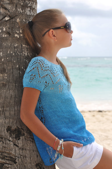 Saona knitted sweater pattern by designer Natalie Pelykh on young girl leaning against a tree at the beach