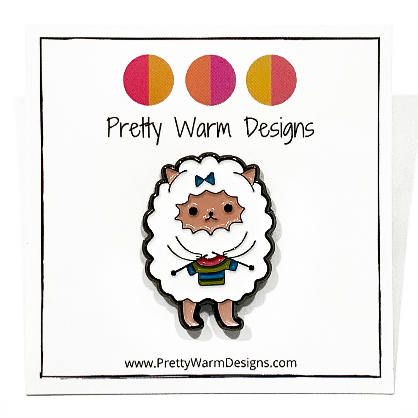 Enamel pin of a white cartoon sheep knitting a rainbow striped sweater, on Pretty Warm Designs backing card