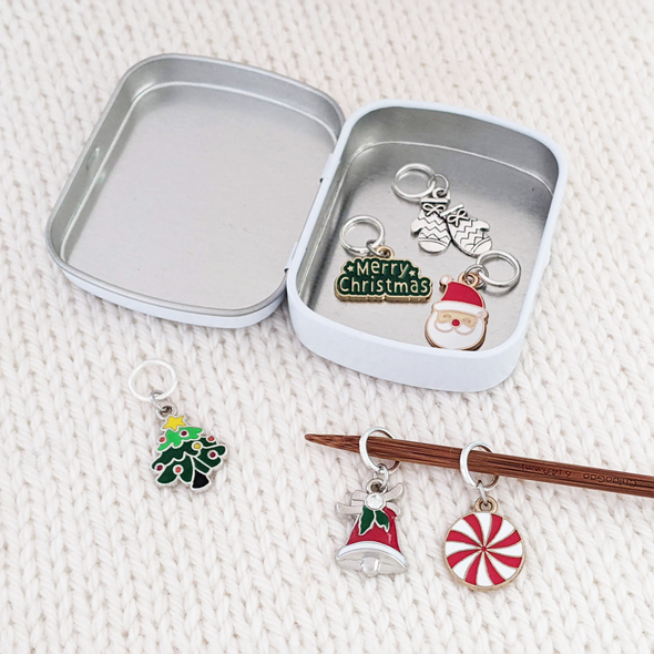 Set of 6 metal alloy and enamel Christmas stitch markers with storage tin, ring style for knitting. Includes "Merry Christmas", peppermint, Christmas tree, Santa, Mittens, and Bell