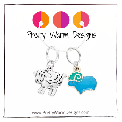 Two knitting ring stitch markers, one enamel blue and green sheep and one Tibetan antiqued silver lamb attached to cardstock with Pretty Warm Designs text and logo