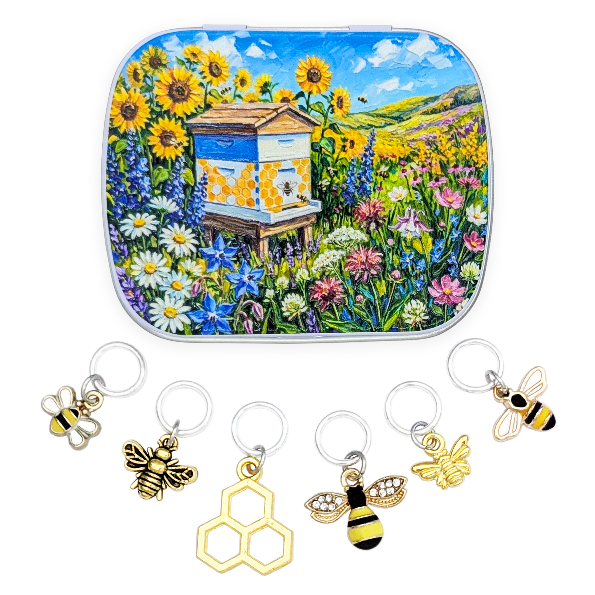 A square metal tin with rounded corners featuring a colorful painted scene of a beehive in a sunflower and wildflower field. Below the tin are six bee-themed riing style stitch markers for knitters.