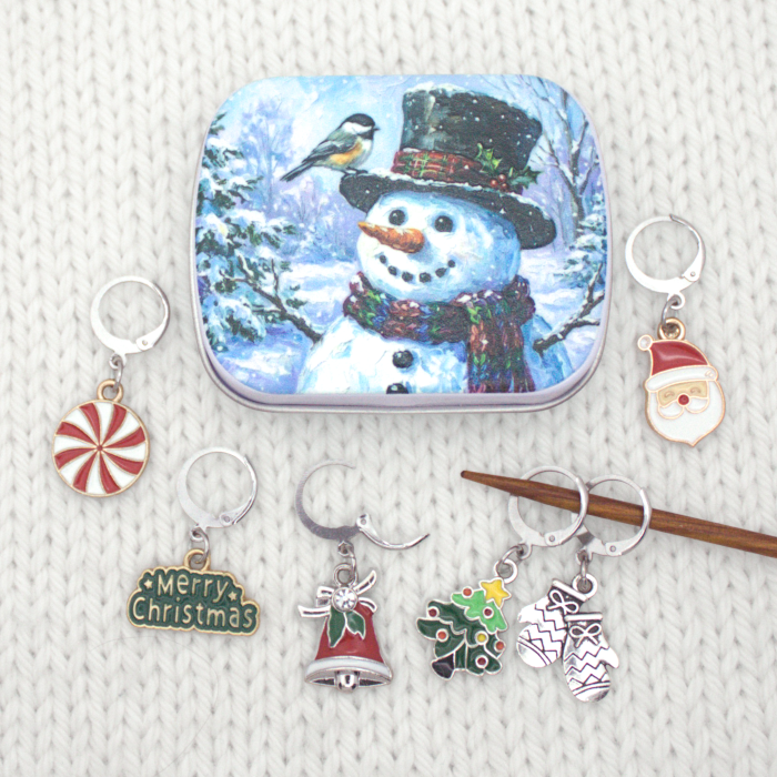 Snowman tin with Christmas locking stitch markers laid out beside it