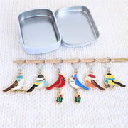 Open silver tin above a row of Christmas bird locking stitch markers