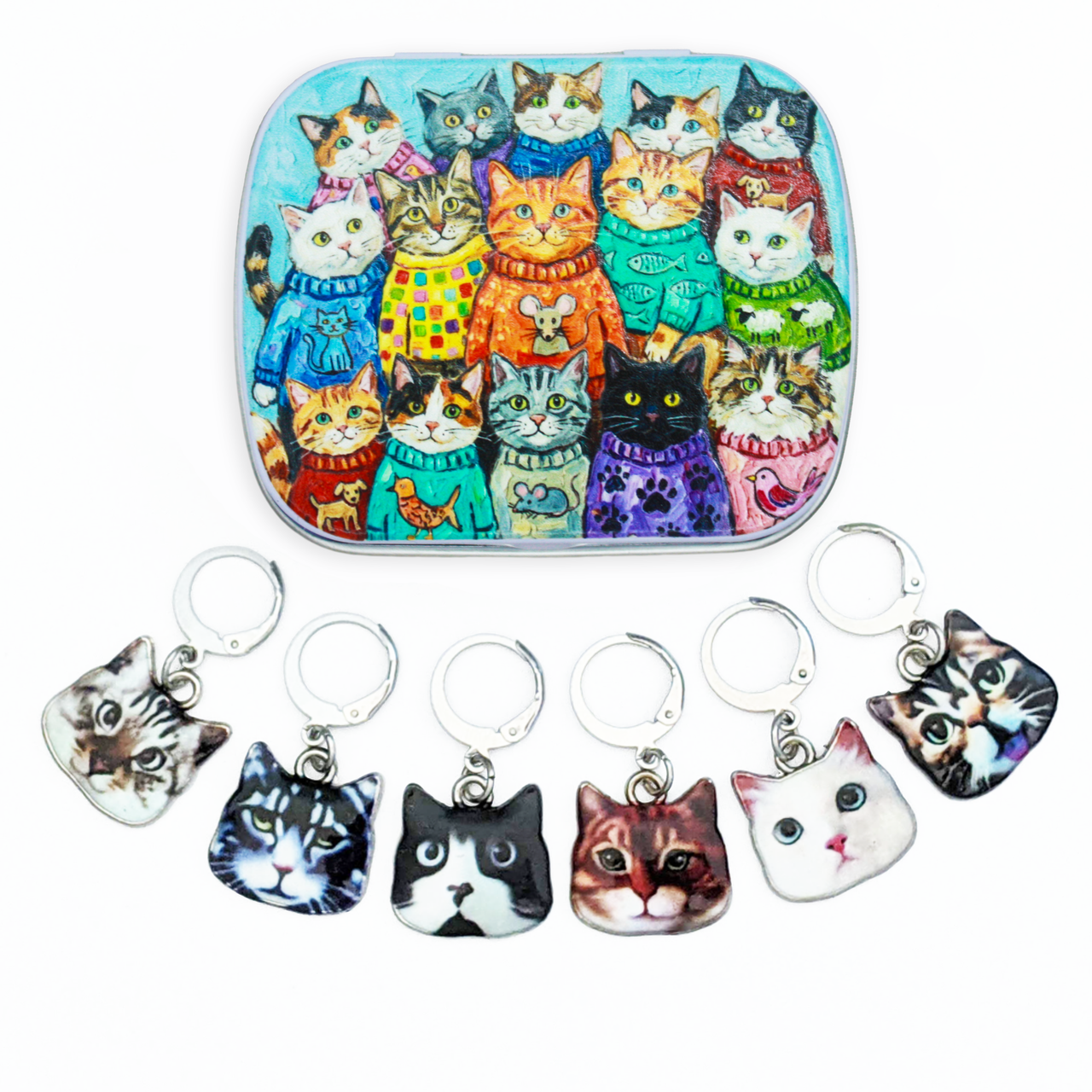 A hinged metal notions tin filled with colorful illustrated cats wearing sweaters, shown above six small cat-face locking stitch markers with leverback clasps on a white background.