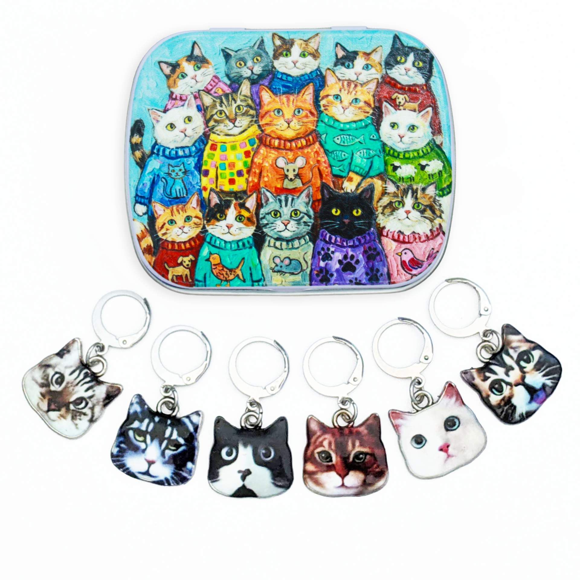 A hinged metal notions tin filled with colorful illustrated cats wearing sweaters, shown above six small cat-face locking stitch markers with leverback clasps on a white background.