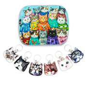 A hinged metal notions tin decorated with a colorful illustration of many cats wearing sweaters, shown above six ring style stitch markers with cat face charms, against a plain white background.