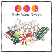 Close-up of six enamel Christmas charm stitch markers: peppermint, tree, Santa, bell and more