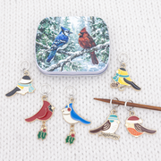 Christmas bird stitch markers beside the tin with wooden knitting needles