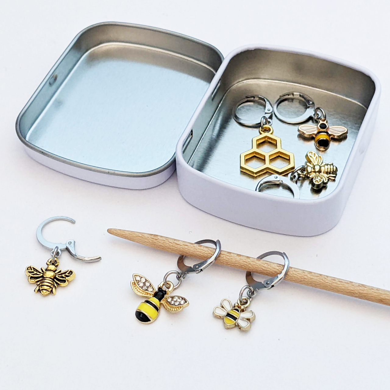 Set of 6 bee themed enamel charms locking crochet stitch markers for crochet shown with storage tin and knitting needle by Pretty Warm Designs