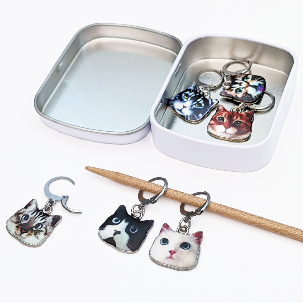 Set of six cat charms locking stitch holders with decorative tin for crochet and knitting by Pretty Warm Designs, shown on knitting needle