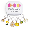 Set of six white, yellow and green enamel metal daisy charms with lever back clasps stitch markers for crochet and decorative tin with logo by Pretty Warm Designs