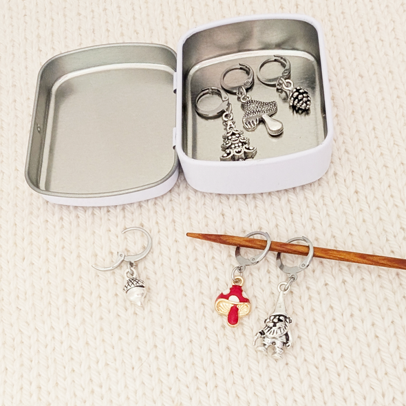 Set of five antiqued silver charm crochet stitch markers and one enamel toadstool charm locking crochet stitch markers with decorative Pretty Warm Designs logo tin for crochet by Pretty Warm Designs