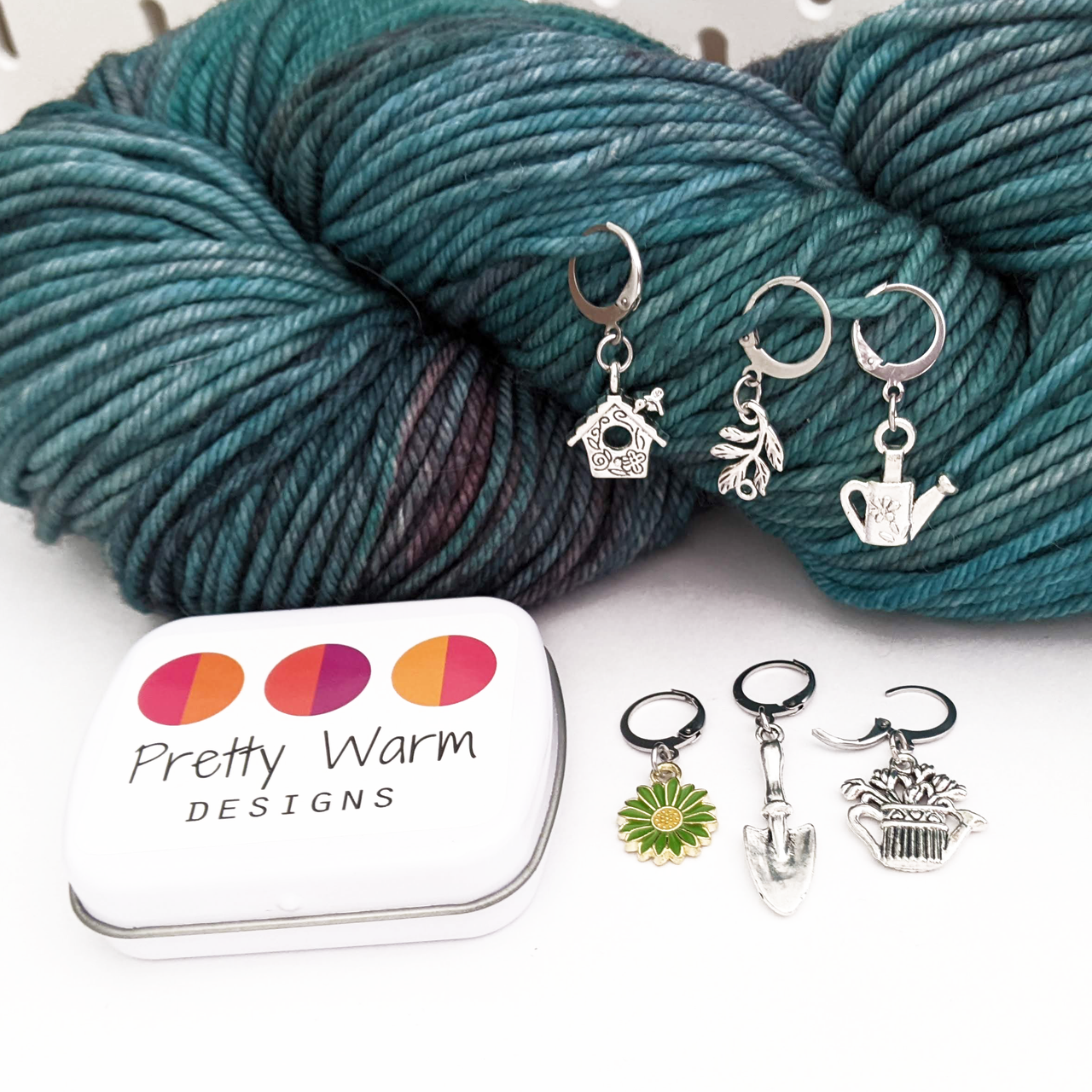 Set of one green and yellow enamel daisy and five antiqued silver alloy gardening themed locking stitch markers with a green worsted weight skein of yarn for crochet by Pretty Warm Designs Inc