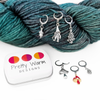 Set of five antiqued silver charm crochet stitch markers and one enamel toadstool charm locking crochet stitch markers with decorative Pretty Warm Designs logo tin for crochet by Pretty Warm Designs