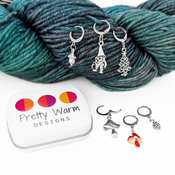 Set of five antiqued silver charm crochet stitch markers and one enamel toadstool charm locking crochet stitch markers with decorative Pretty Warm Designs logo tin for crochet by Pretty Warm Designs