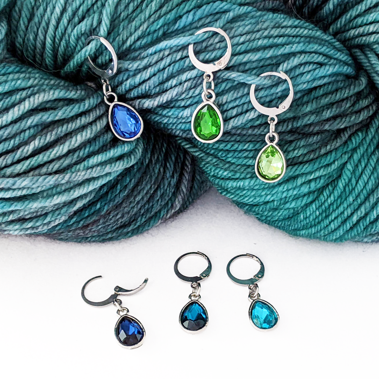 Ocean Waters locking stitch marker set of 6 with storage tin. Removable leverback clasps for crochet or knitting. Shown on worsted weight yarn.