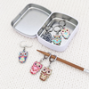 Set of six multicolored enamel on silver toned alloy owl locking stitch markers for crochet with decorative tin by Pretty Warm Designs, shown with knitting needle
