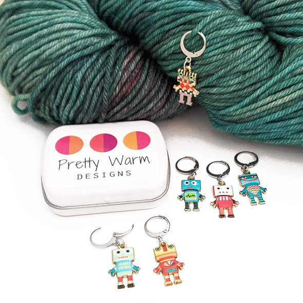 Set of 6 robot themed stitch markers for crochet or knitting, shown with storage tin a worsted weight yarn.