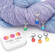 Rainbow Sparkle Crochet Stitch Markers, Set of 6 with storage tin. 6 different pride colors with a leverback clasp for knitter or crocheters. Shown attached to worsted weight yarn.
