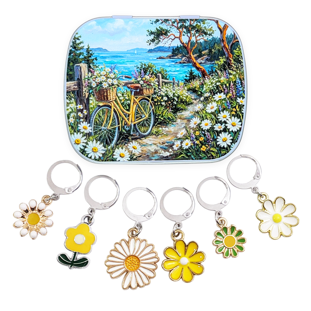 A hinged metal notions tin featuring a colorful landscape illustration of a yellow bicycle on a flower-lined path by the sea, shown above six matching flower-shaped locking stitch markers for knitters or crocheters