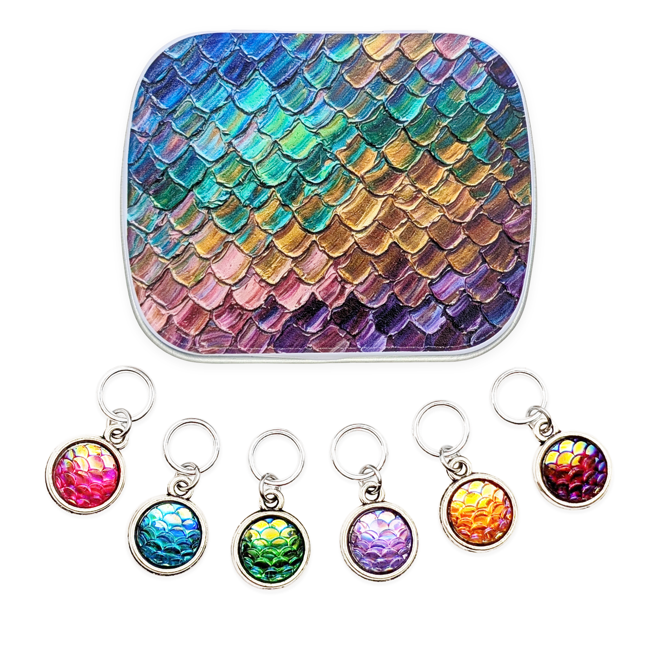 A hinged notions tin with featuring an iridescent mermaid scale pattern in blue, green, gold, pink, and purple, shown above six matching circular resin charm ring markers with silver rings on a white background.