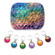 A hinged notions tin with featuring an iridescent mermaid scale pattern in blue, green, gold, pink, and purple, shown above six matching circular resin charm ring markers with silver rings on a white background.