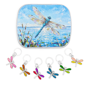 A square tin with rounded corners featuring a painted blue dragonfly over water, shown above five small dragonfly-shaped ring style stitch marker charms in different colors attached to silver rings on a white background.