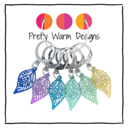 A set pf six locking stitch markers for crochet or knitting with colourful lightweight filigree metal charms in the shape of leaves.