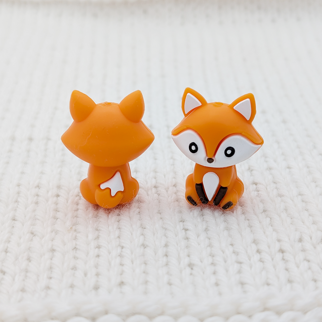Front and back view of sculpted Crafty Fox stitch stoppers on white knit fabric, showing full 3D detail including fluffy tail