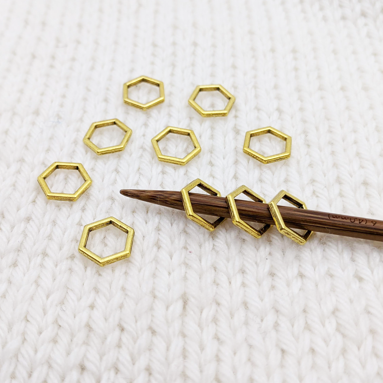 Set of 10 gold toned hexagon metal stitch markers for knitting shown on 4mm knitting needle.