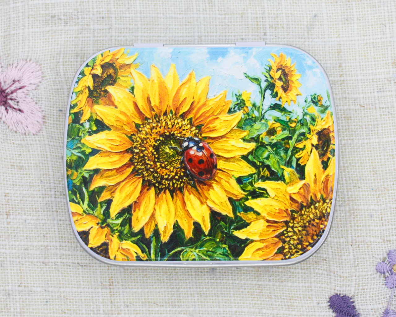 A metal notions tin for craft storage with yellow sunflowers and a red ladybug on the lid
