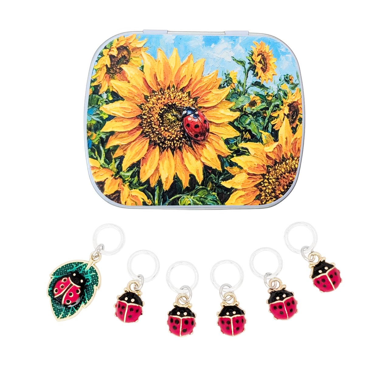 A small notions tin featuring a colorful sunflower and ladybug illustration, shown above six matching ladybug-shaped stitch markers on silver-toned rings against a white background.