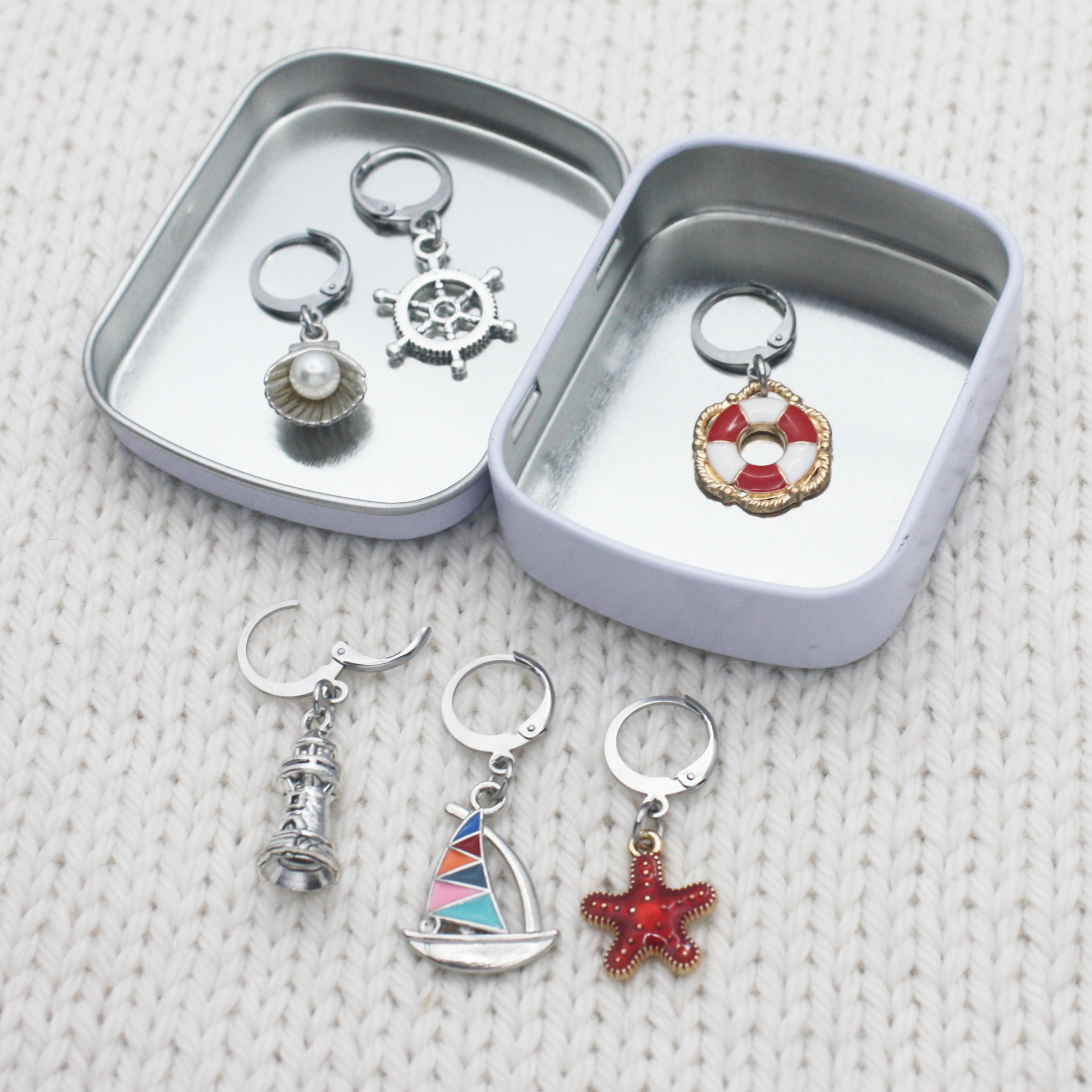 Travel-friendly hinged storage tin for fiber arts accessories, displaying a complete six-piece set of coastal theme clasp markers.