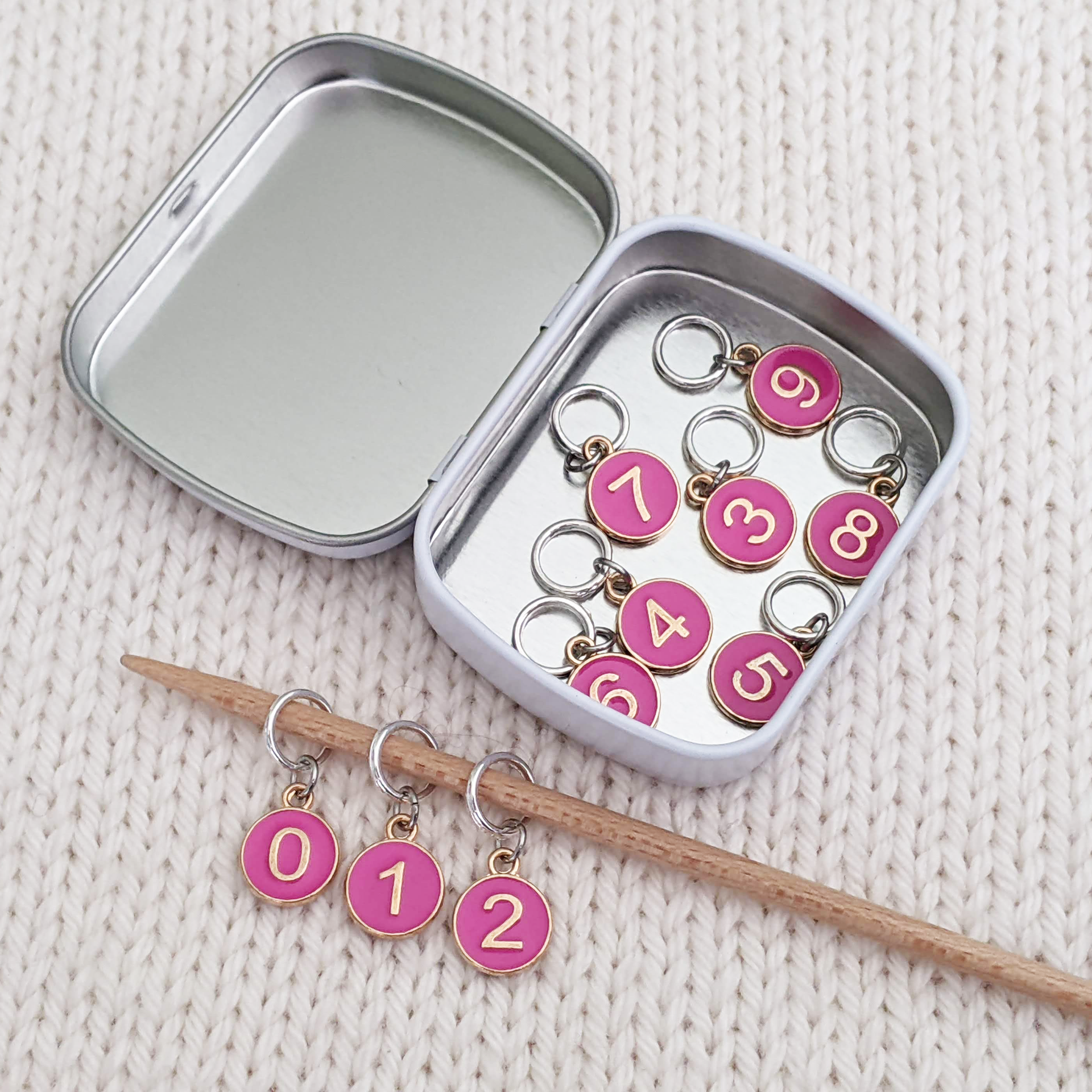 Dusky Rose Numbered Stitch Markers set of 10 with storage tin displayed on bamboo knitting needle and inside storage tin