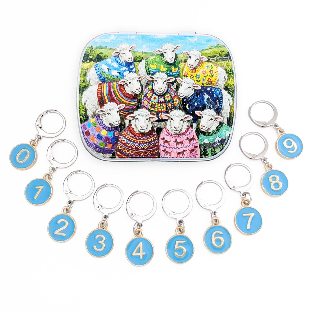 A set of 10 locking stitch markers with blue circular discs numbered 0 to 9, arranged around a matching decorative metal tin featuring a colorful illustration of sheep in knitted sweaters on a white background.