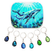 A hinged metal notions tin with a humpback whale print with six locking stitch markers in blues and greens