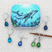 A yarn accessories notions tin with a humpback whale & calf print and six locking stitch holders