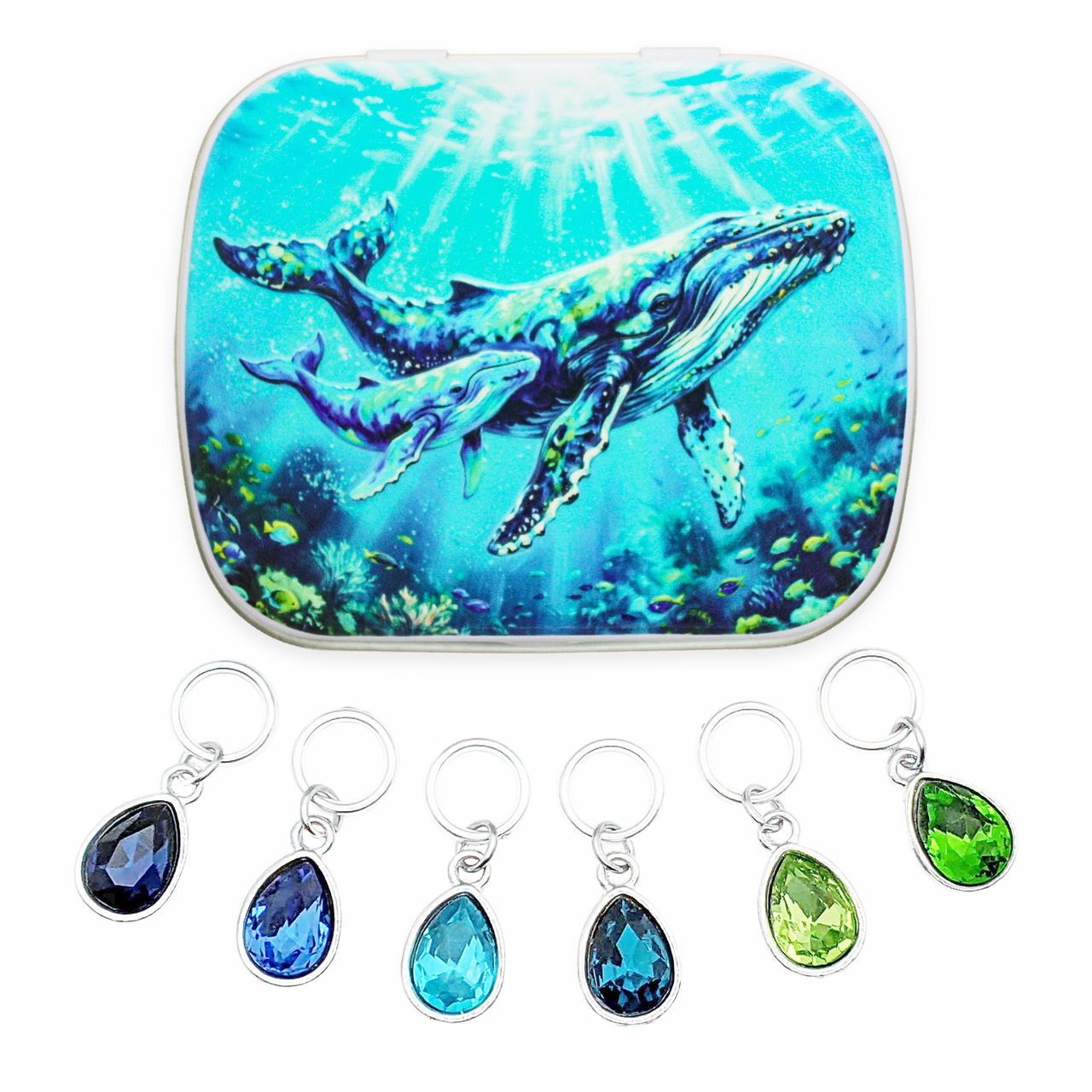 A craft notions tin with an underwater humpback whale and calf print in blue and green tones, and 6 ring stitch makers for knitting with teardrop-shaped faceted gemstones in ocean shades