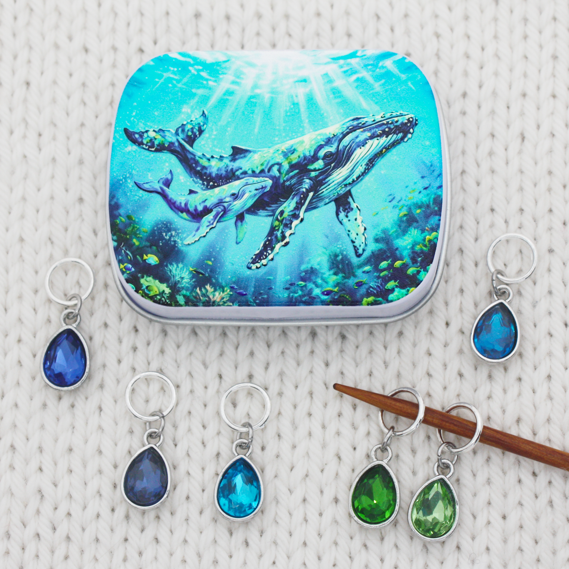 A fiber arts notions tin with an humpback whale and calf print and a set of 6 ring stitch makers for knitting with teardrop crystal glass charms in blues and greens
