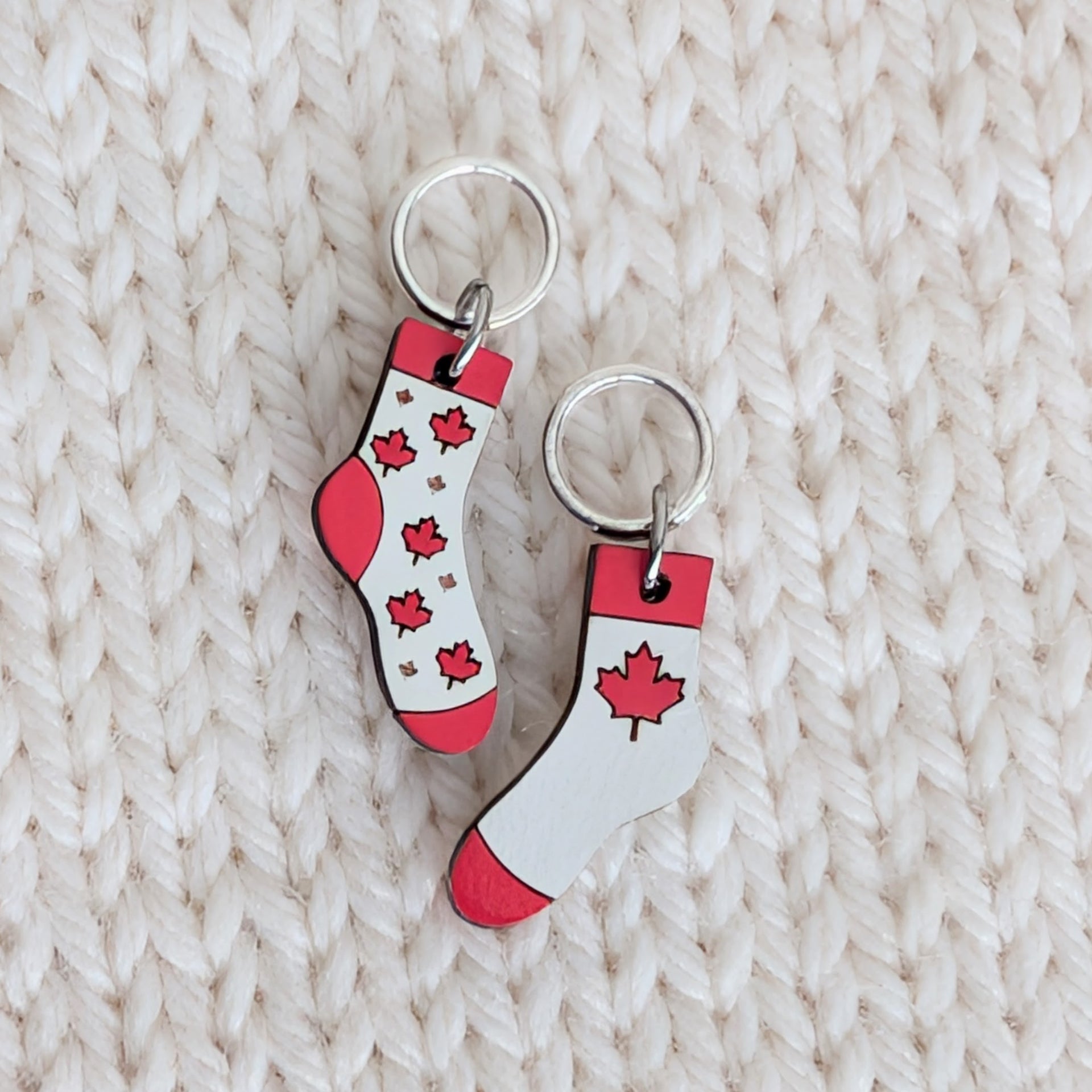 Close-up of Canadian-made Maple Leaf Socks knitting stitch markers handcrafted from basswood. The hand-painted sock-shaped charms feature smooth, silver-toned closed rings that easily slide over knitting needles up to US 8 (5mm).