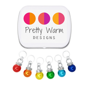 Rainbow Sparkle Set of 6 Stitch Markers, Ring Style for Knitting, including storage tin. Colors include red, orange, yellow, green, blue, and indigo. Charms include a sparkly rhinestone collar.