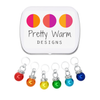 Rainbow Sparkle Set of 6 Stitch Markers, Ring Style for Knitting, including storage tin. Colors include red, orange, yellow, green, blue, and indigo. Charms include a sparkly rhinestone collar.