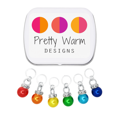 Rainbow Sparkle Set of 6 Stitch Markers, Ring Style for Knitting, including storage tin. Colors include red, orange, yellow, green, blue, and indigo. Charms include a sparkly rhinestone collar.
