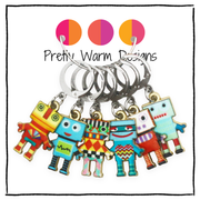 Six colorful robot charm locking stitch markers displayed against a white background with three circular color swatches and the text 'Pretty Warm Designs' at the top.
