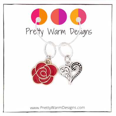 Two Valentine's Day themed knitting ring stitch markers, one red rose and one Tibetan antiqued silver filigree heart with Pretty Warm Designs text and logo