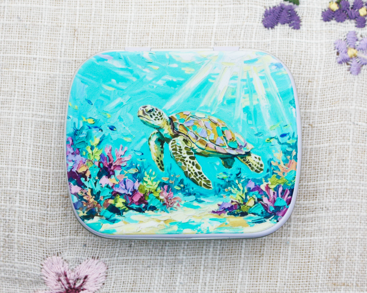 A hinged notions tin for yarn accessories with a painted sea turtle underwater scene