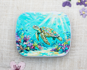 A hinged notions tin for yarn accessories with a painted sea turtle underwater scene