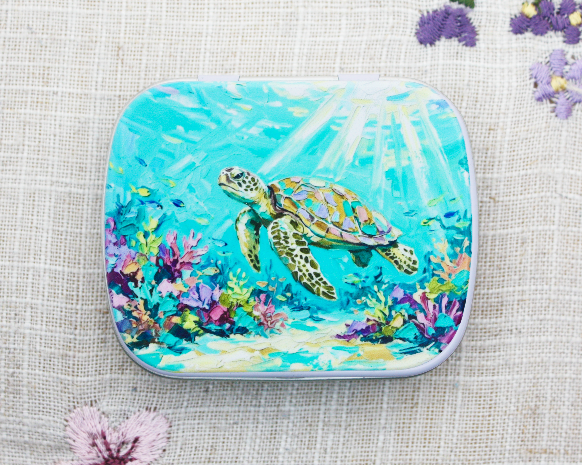 A hinged notions tin for yarn accessories with a painted sea turtle underwater scene
