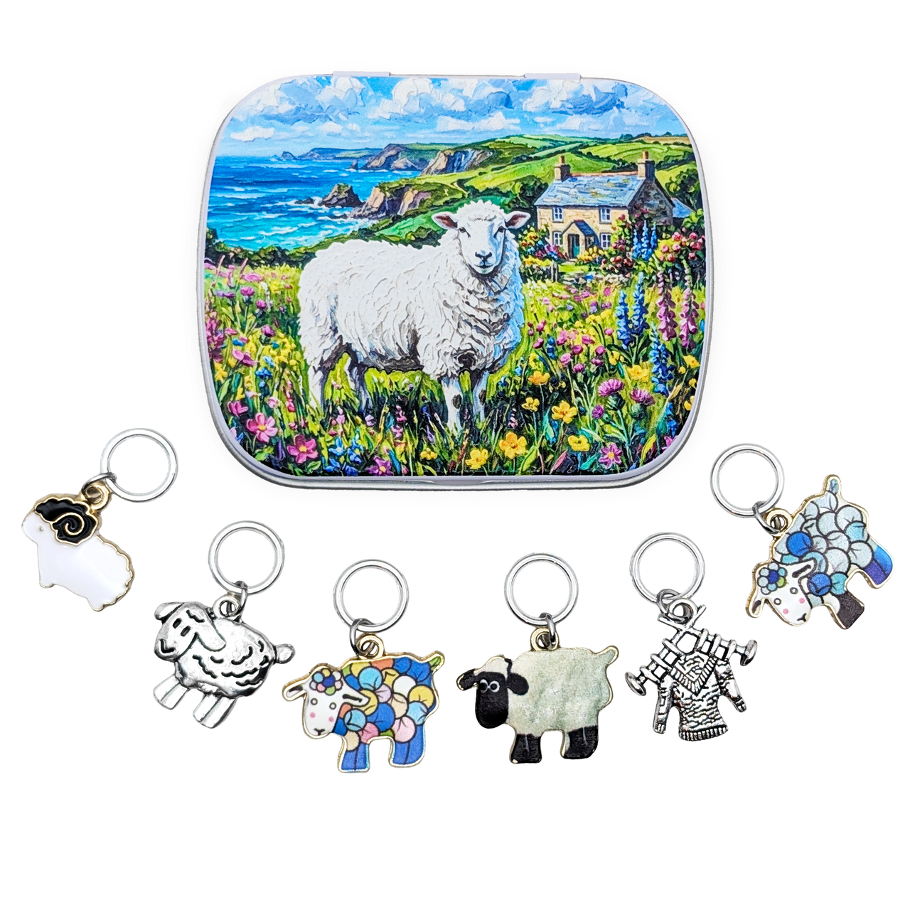 A square tin with rounded corners featuring a colorful illustration of a white sheep standing in a flower field near a cottage and the sea. Below the tin are six small metal ring style stitch markers for knitters, with charms shaped like sheep and a lamb, shown on a plain white background.